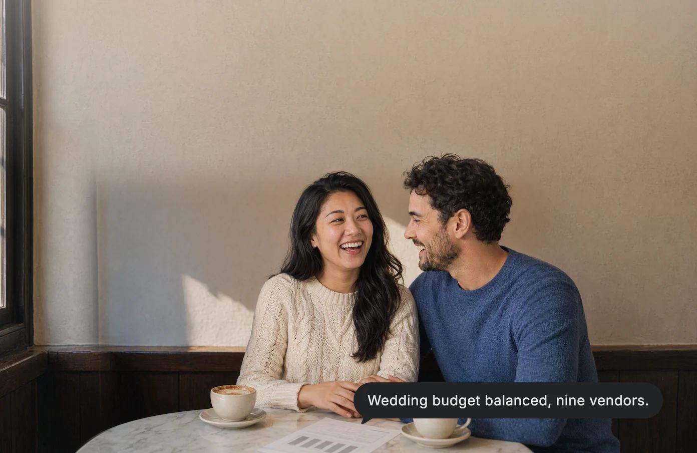 A couple laughs at a café table over the printed wedding budget; Dvina’s answer: Wedding budget balanced, nine vendors.