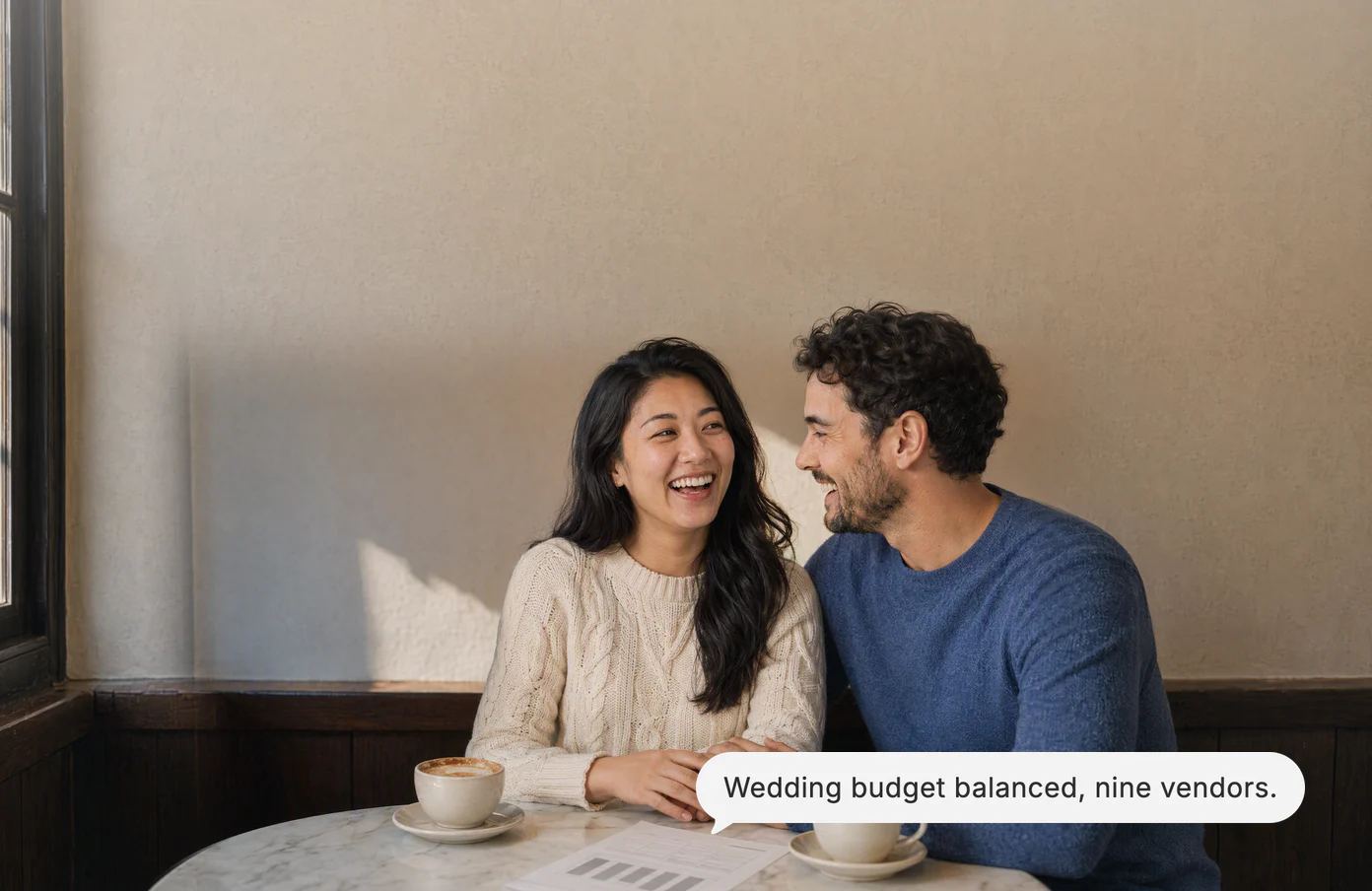 A couple laughs at a café table over the printed wedding budget; Dvina’s answer: Wedding budget balanced, nine vendors.