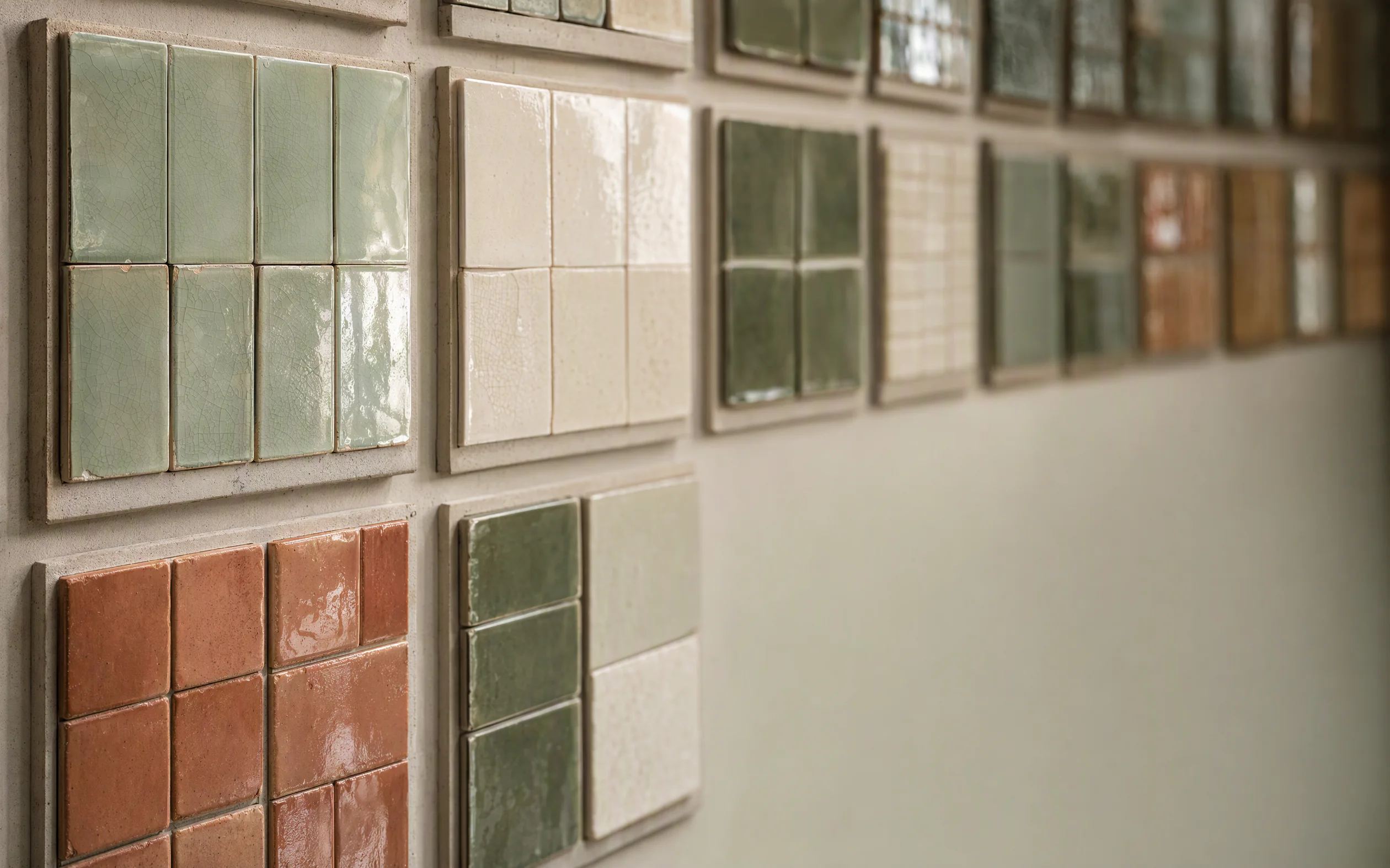 A wall of glazed tile samples in a showroom, sage greens, whites and terracotta in soft daylight.