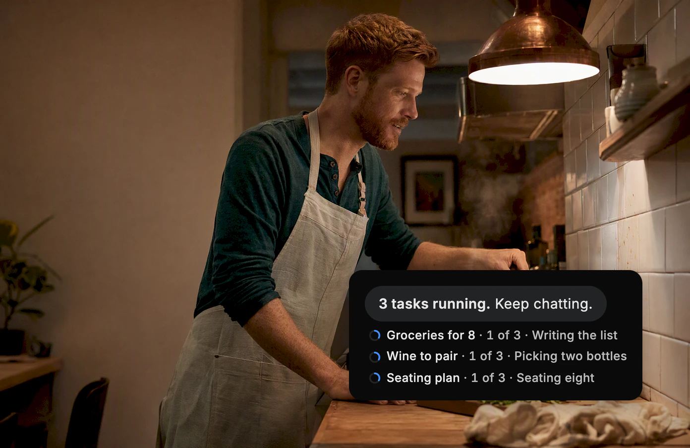 A man stirs a pot at his stove, his phone propped up beside him. Dvina: 3 tasks running. Keep chatting. Groceries for 8, Wine to pair and Seating plan are underway.