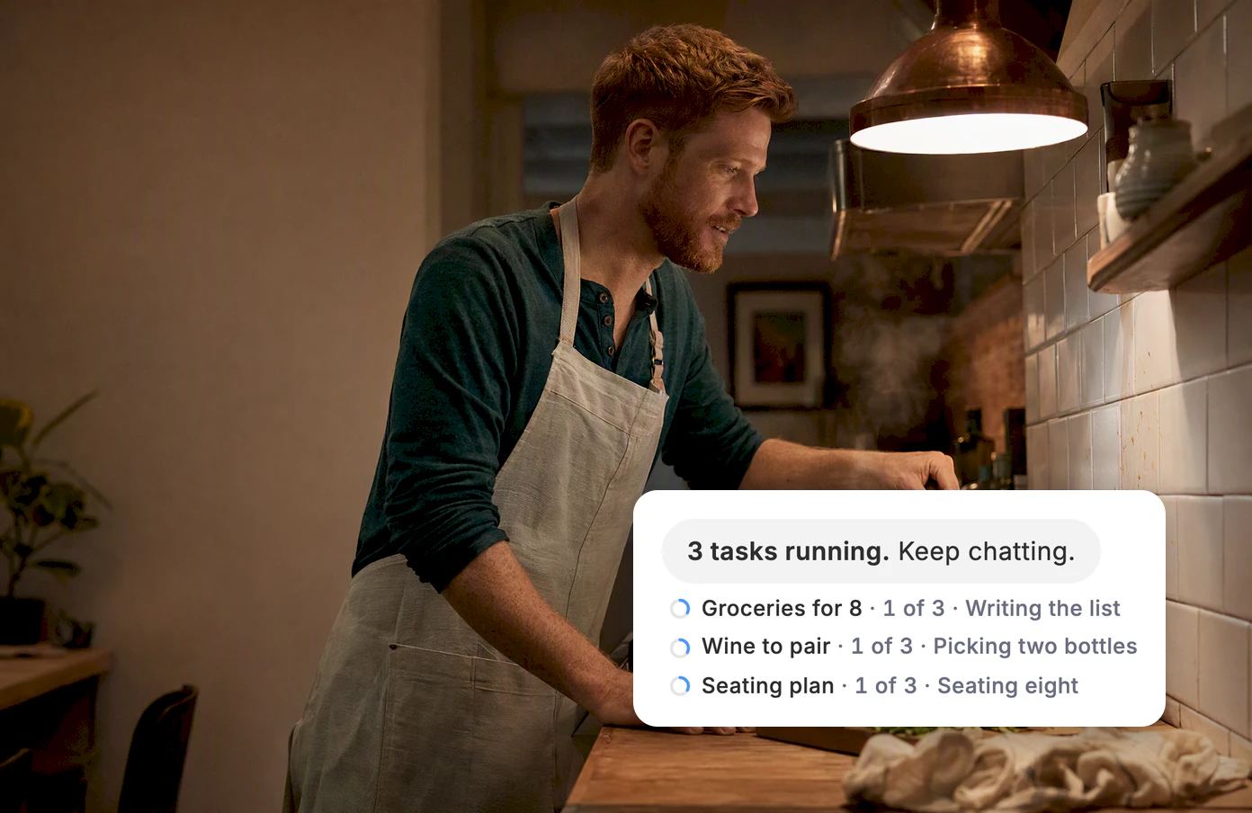 A man stirs a pot at his stove, his phone propped up beside him. Dvina: 3 tasks running. Keep chatting. Groceries for 8, Wine to pair and Seating plan are underway.
