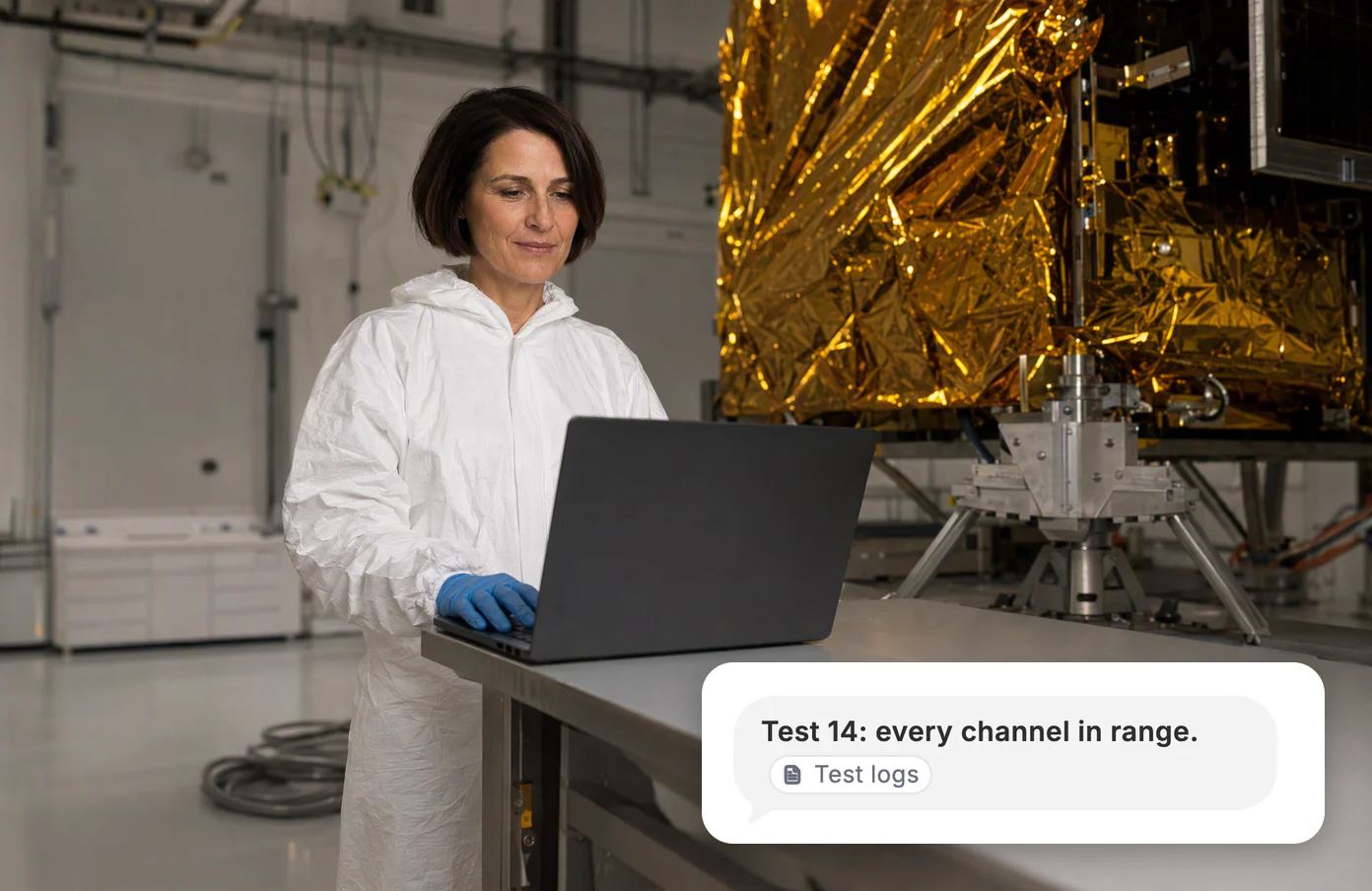 A test engineer at a bench beside a satellite wrapped in gold foil. Dvina: test 14, every channel in range, from the test logs.