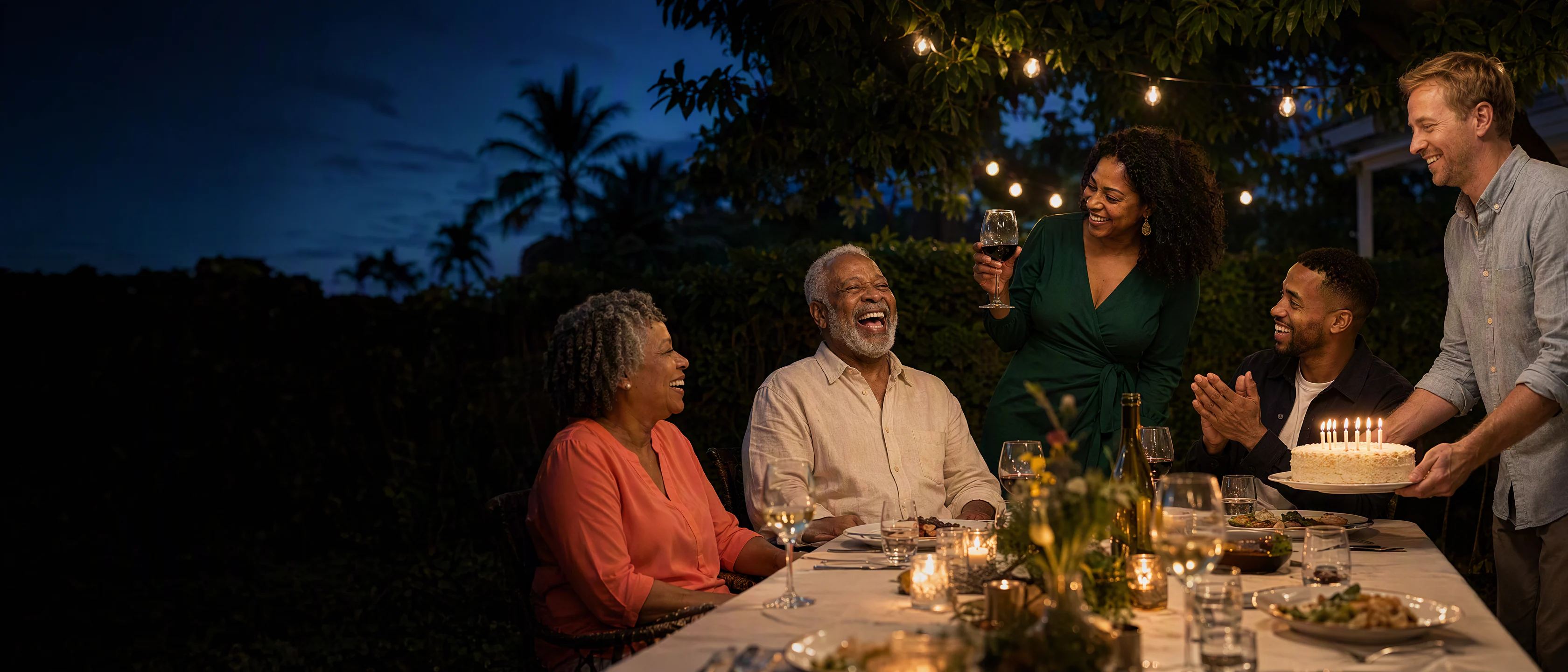 A backyard under string lights at dusk: Leon laughs as his daughter Celine raises a glass, the family around the table and the cake arriving.