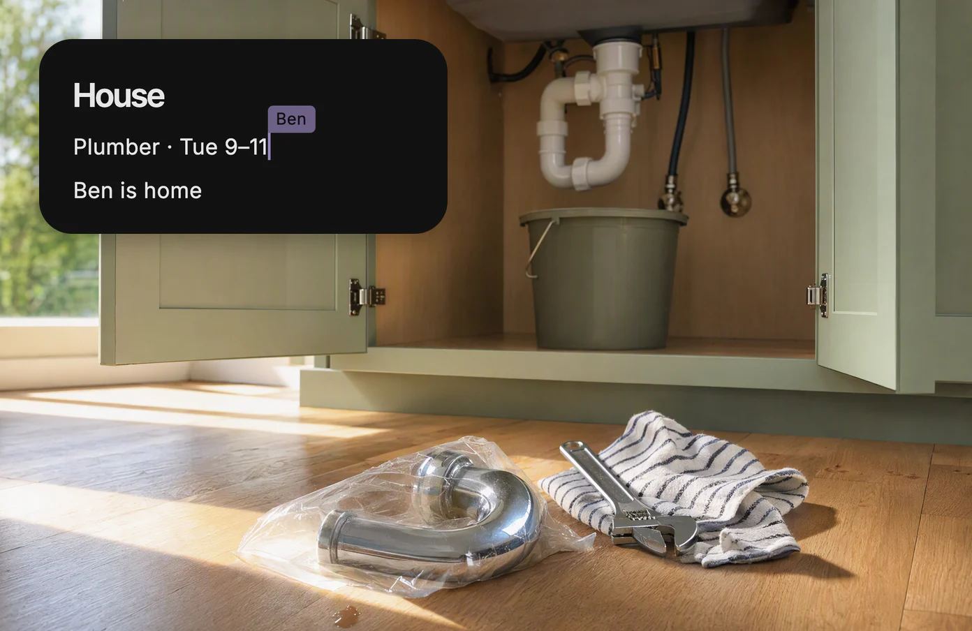 An open sink cabinet with a wrench and a new pipe, with the shared page House: Plumber Tuesday 9 to 11, Ben is home.