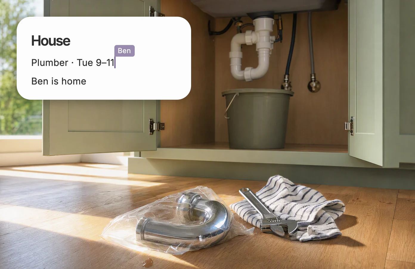 An open sink cabinet with a wrench and a new pipe, with the shared page House: Plumber Tuesday 9 to 11, Ben is home.