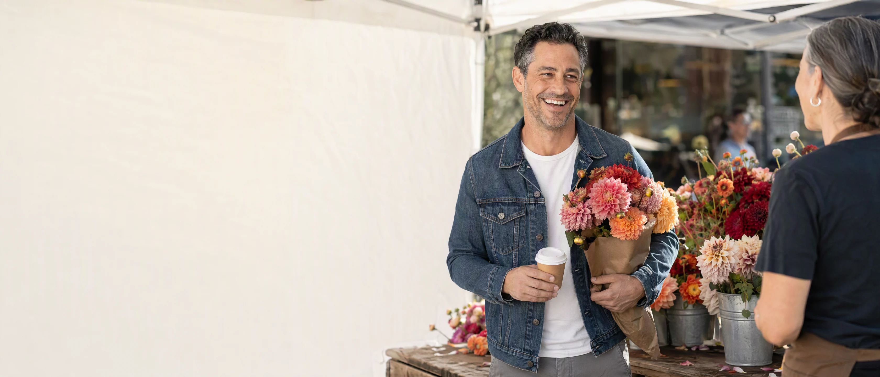 A Saturday farmers market: Spencer, coffee in hand and dahlias under his arm, laughs with the flower seller.