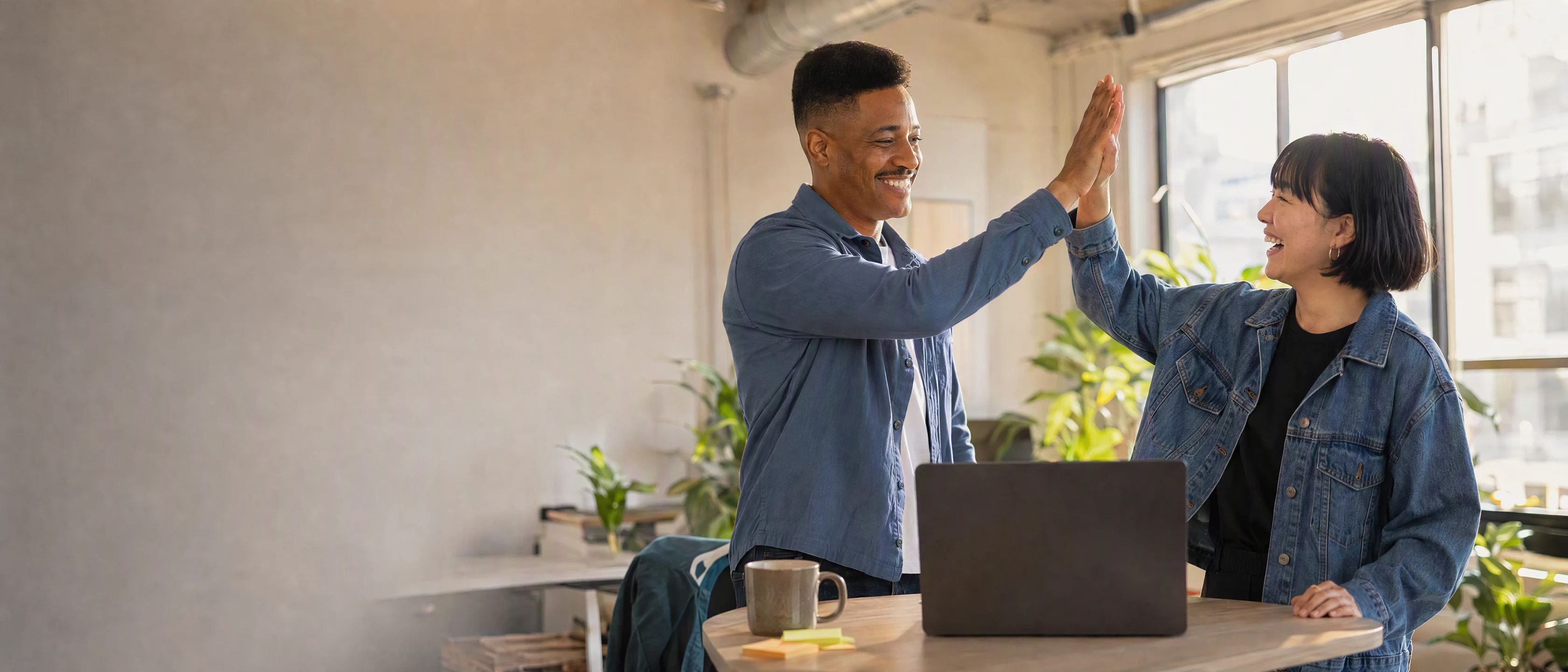 A bright startup office: Jordan and Mei high-five at the standing desk as the deploy goes green.