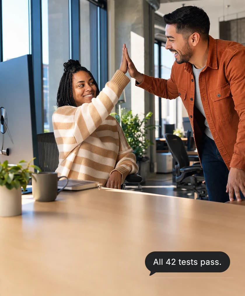 Twee ontwikkelaars geven elkaar een high five aan het bureau van de vrouw terwijl de testronde wordt afgerond. Kaart van Dvina: Alle 42 tests geslaagd.