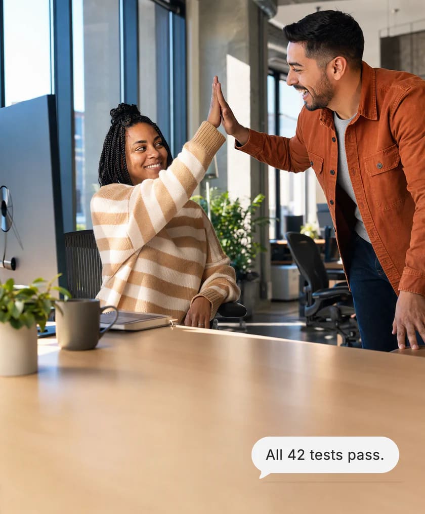 Twee ontwikkelaars geven elkaar een high five aan het bureau van de vrouw terwijl de testronde wordt afgerond. Kaart van Dvina: Alle 42 tests geslaagd.
