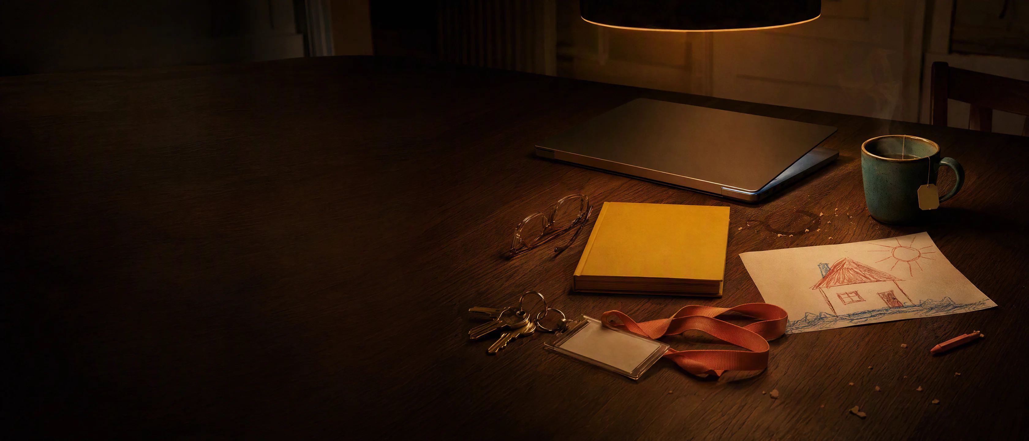 A kitchen table at 10 PM under one lamp: a laptop half closed, a library book, a child’s drawing, car keys, a mug and a folded hospital lanyard.