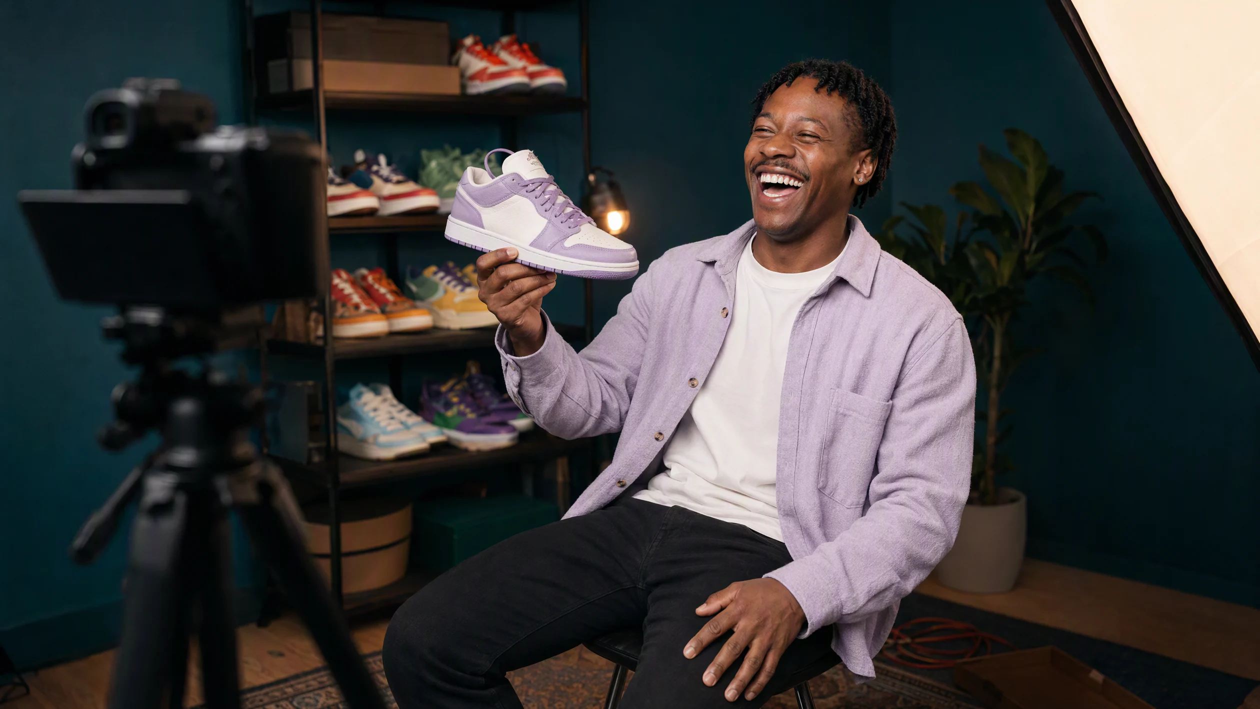 A video creator in his home studio at night, mid-take, holding a sneaker up to his camera and laughing at his own blooper.