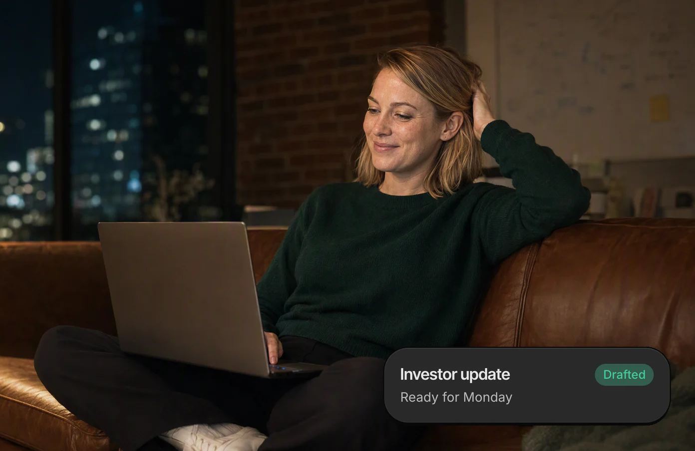 A founder cross-legged on her office sofa on a Sunday night, her laptop on her knees, grinning; her Dvina card: the investor update, drafted and ready for Monday.